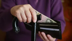 Ruka seniora s holí drží peněženku s českými bankovkami, důchodce a finance.